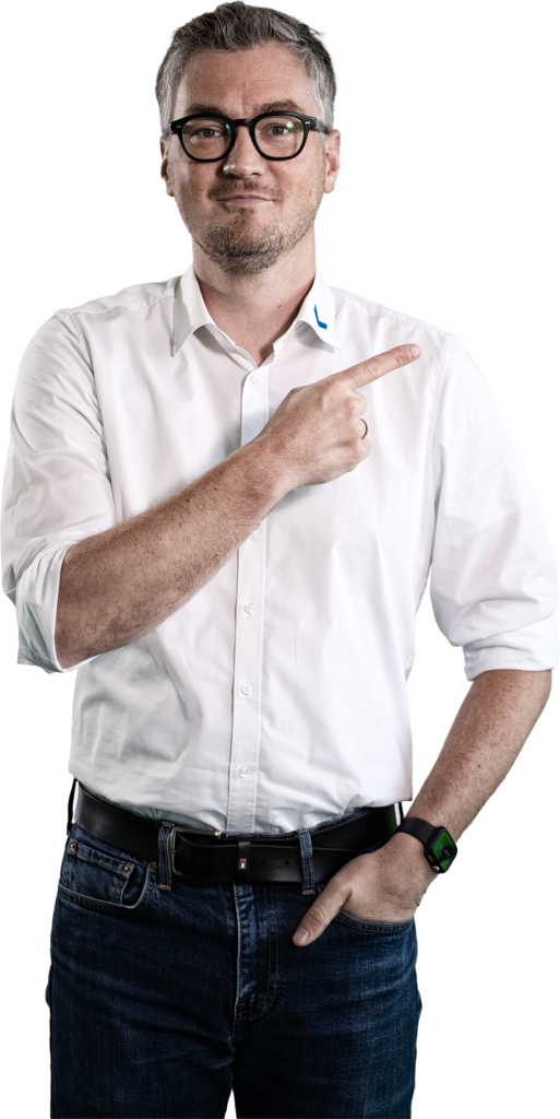 Un uomo in camicia bianca e jeans indica con il dito di lato.