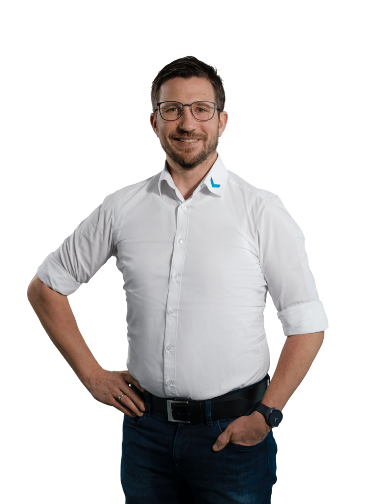 Mann in weißem Hemd mit Brille und Uhr, lächelt in die Kamera.