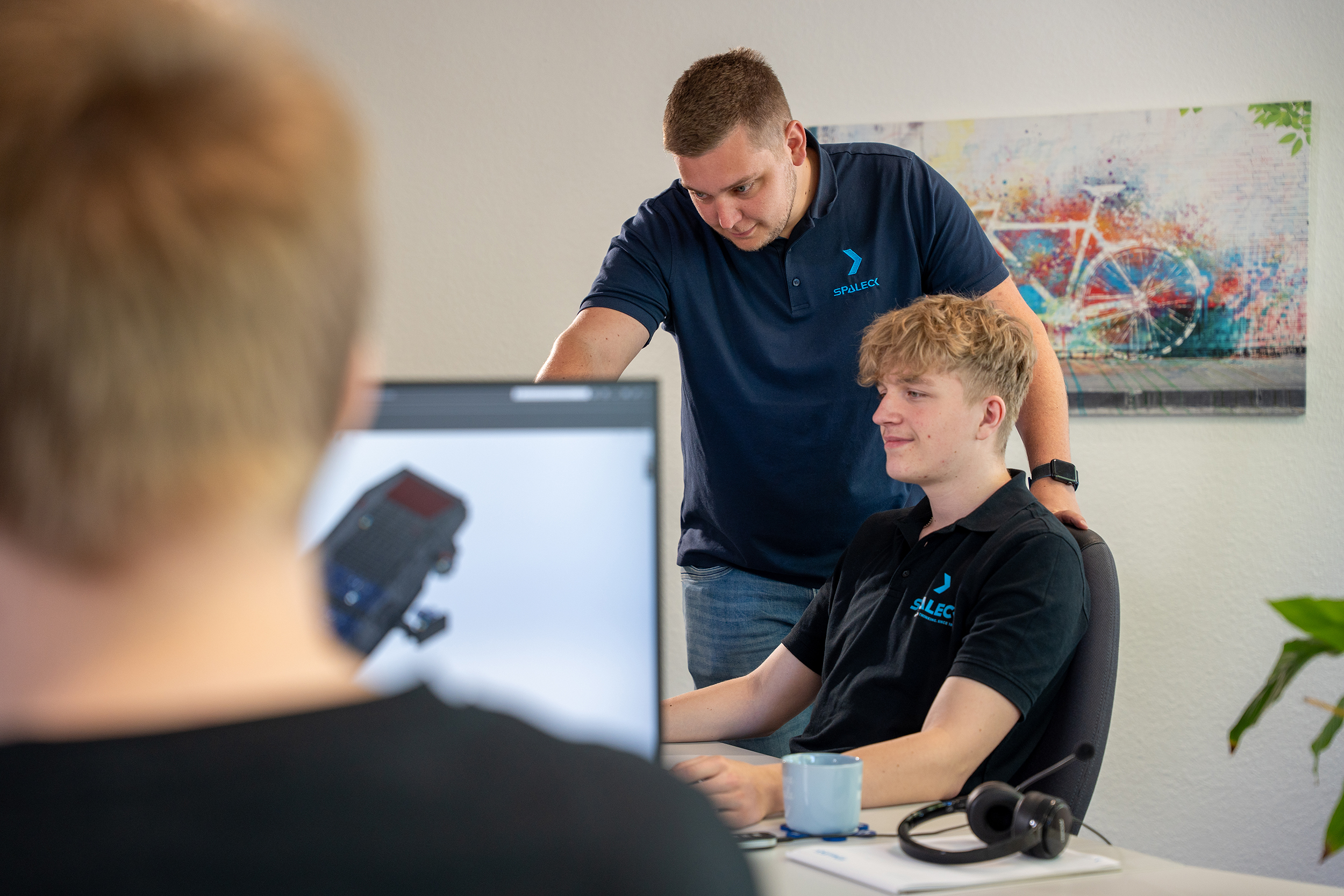 Un collega mostra qualcosa sullo schermo a un apprendista che sta seguendo un corso di formazione per diventare progettista tecnico di prodotti