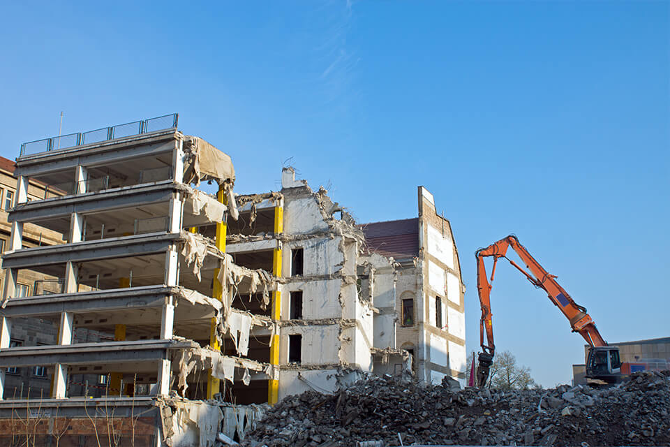 Demolizione di un edificio con un escavatore; in primo piano, rifiuti edili misti.