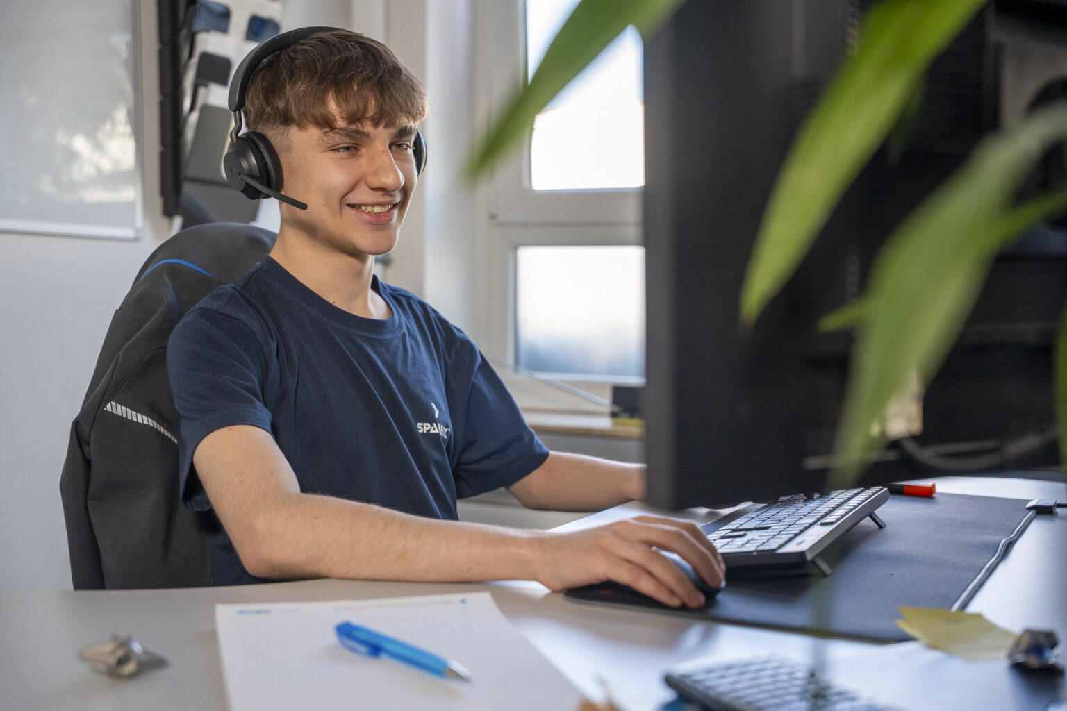 Un apprendista in economia aziendale è seduto alla scrivania e sta parlando al telefono con le cuffie