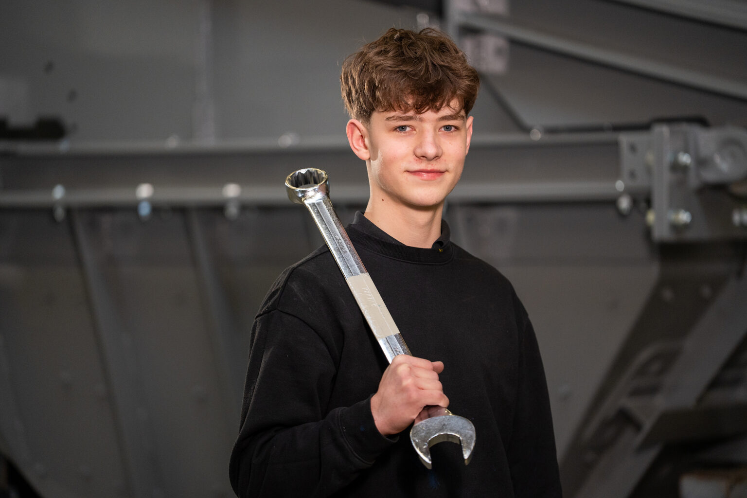 Un ragazzo tiene in mano una grande chiave inglese in un'officina; sta seguendo un percorso di formazione come meccanico industriale.