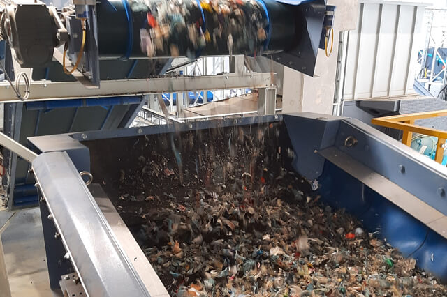 Il materiale cade da un nastro trasportatore in un vaglio ad albero tensionato.