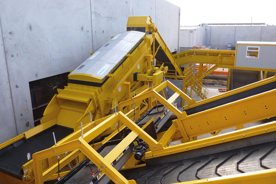 Impianto di riciclaggio giallo per rifiuti edili misti, dotato di nastri trasportatori.