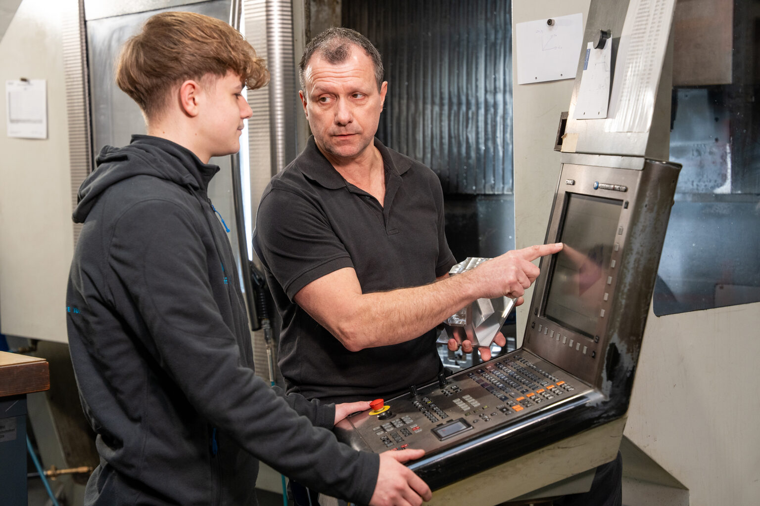 Un istruttore spiega a un ragazzo come funziona una macchina CNC durante il corso di formazione per diventare operatore di macchine utensili.