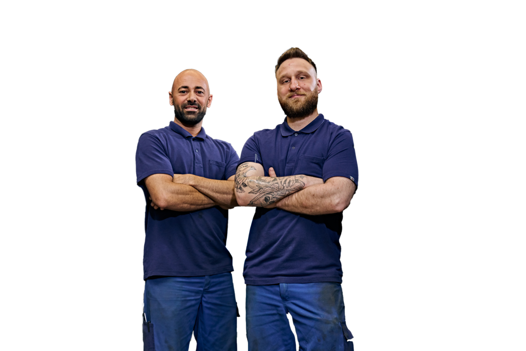 Due uomini in abiti da lavoro stanno uno accanto all’altro con aria sicura.