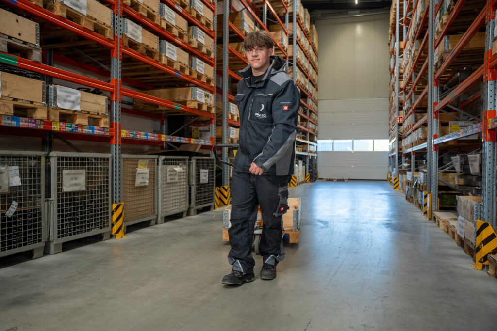 Un apprendista che sta seguendo il percorso formativo per diventare operatore specializzato in logistica di magazzino sposta un transpallet all’interno del magazzino