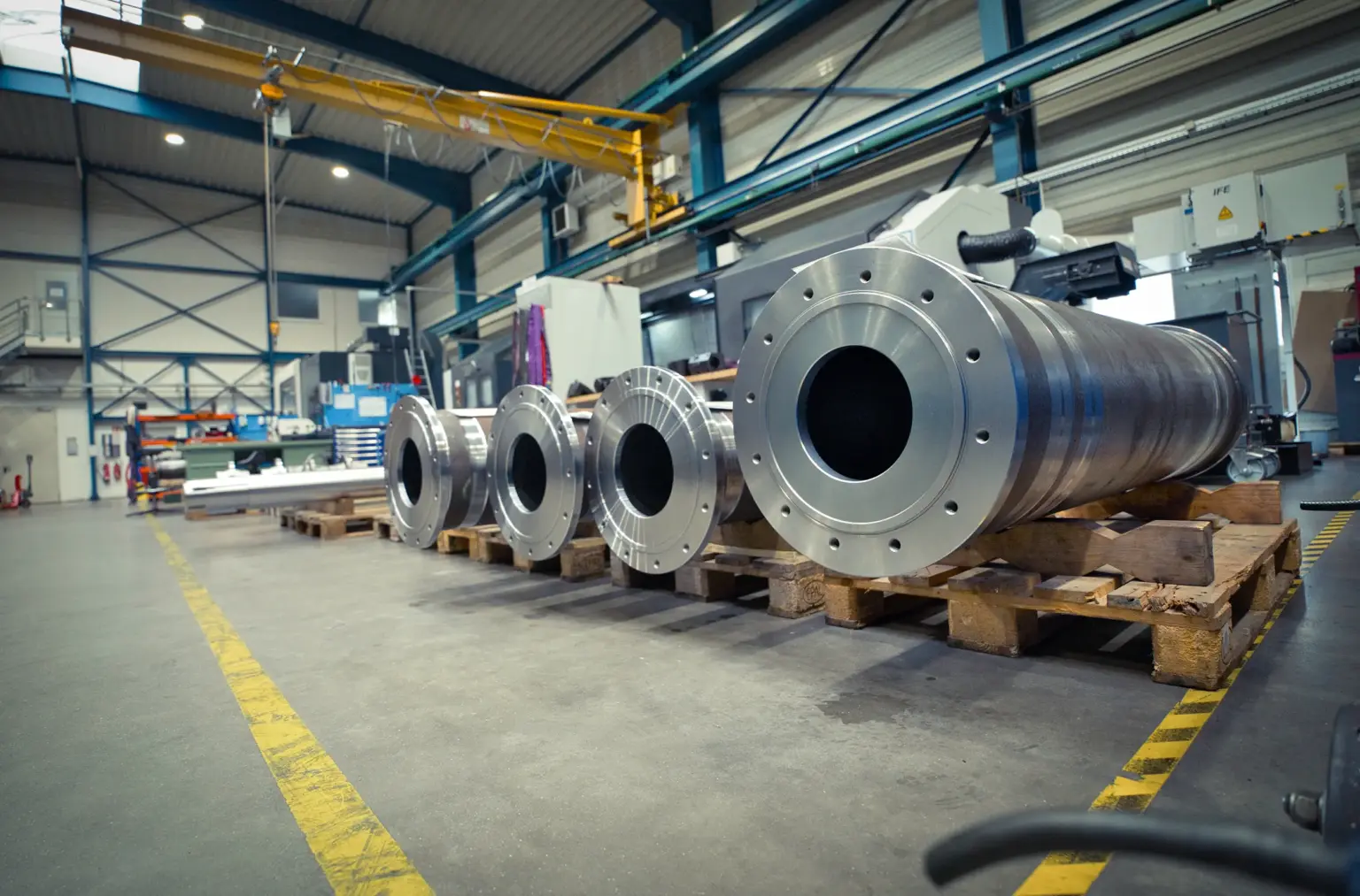 Grandi cilindri metallici su pallet all’interno di un capannone destinato alla lavorazione CNC di pezzi di grandi dimensioni.