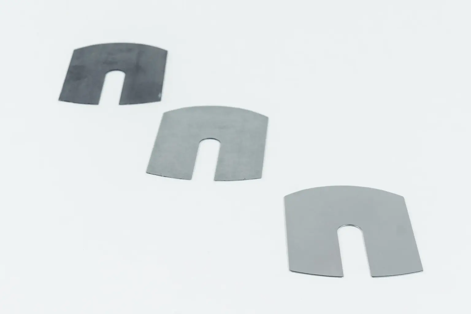 Tre componenti metallici con intagli a forma di U su sfondo bianco.