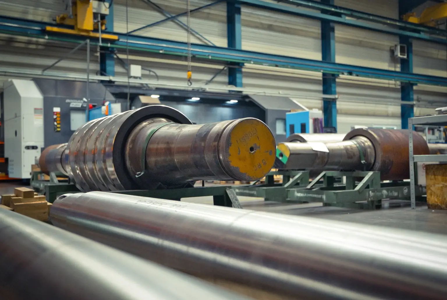 Grandi cilindri metallici in un capannone industriale, adatti alla tornitura di pezzi lunghi.
