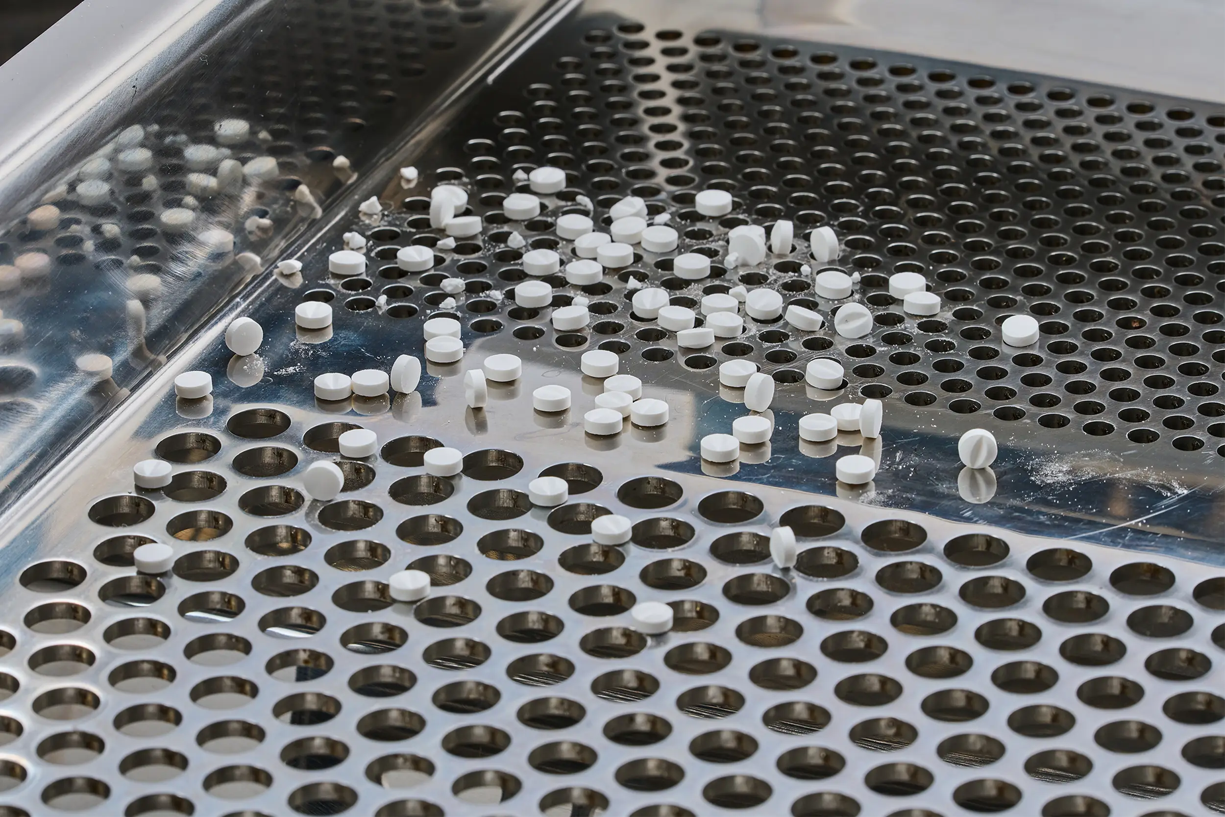 Compresse bianche su un setaccio metallico all’interno di un setacciatore farmaceutico.