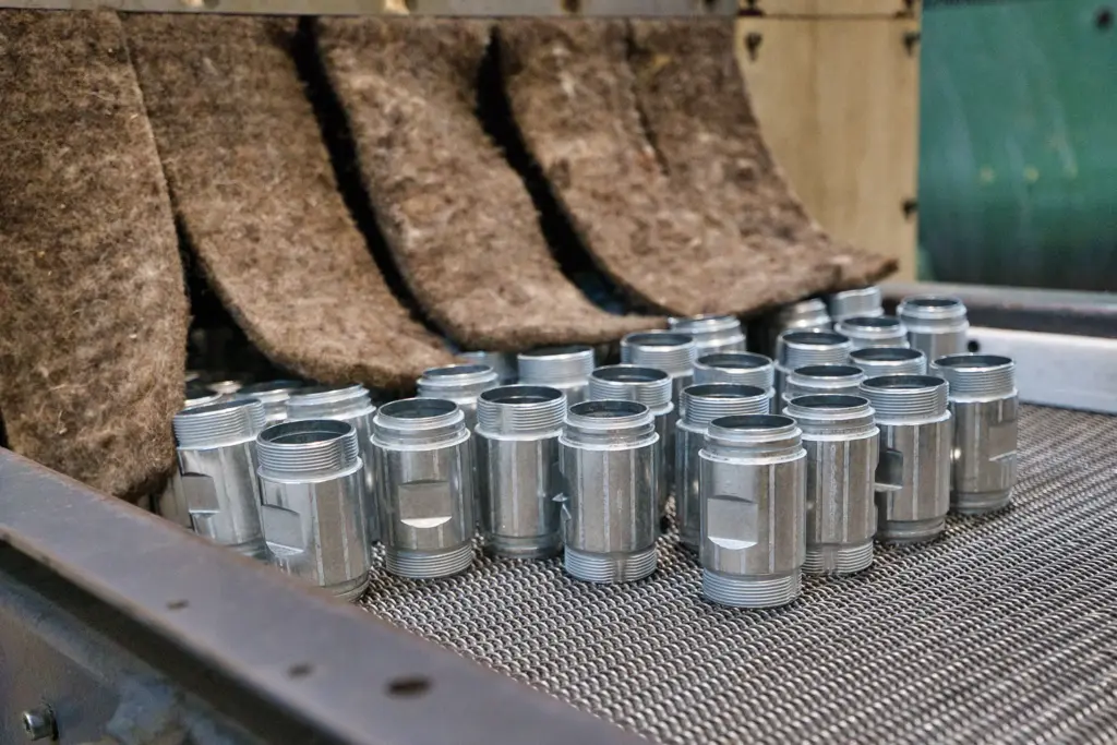 Parti metalliche su un nastro trasportatore all’interno di una levigatrice a vibrazione.
