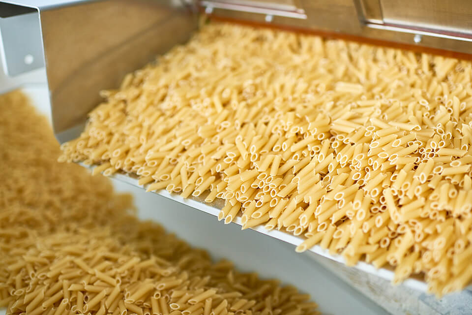 Pasta su un canale vibrante in una linea di produzione.