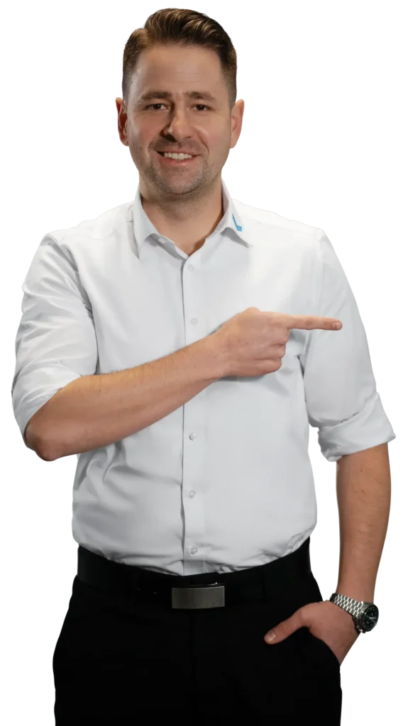 Un uomo in camicia bianca indica verso destra; l'attenzione è focalizzata sulla lavorazione dei metalli.