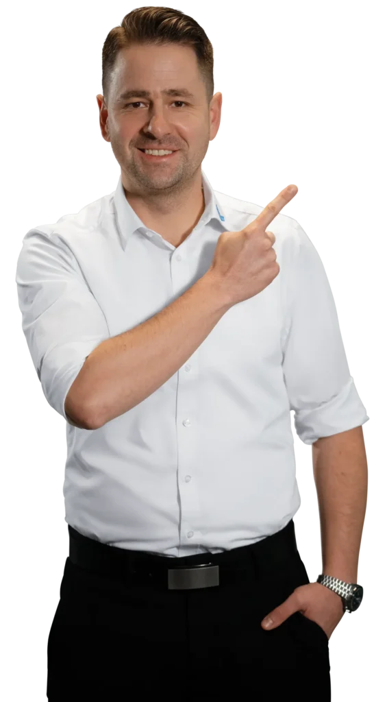 Un uomo in camicia bianca indica sorridendo di lato.