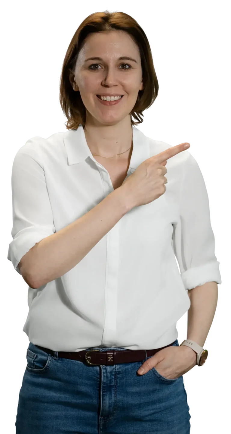Una donna in camicia bianca e jeans indica sorridendo di lato.