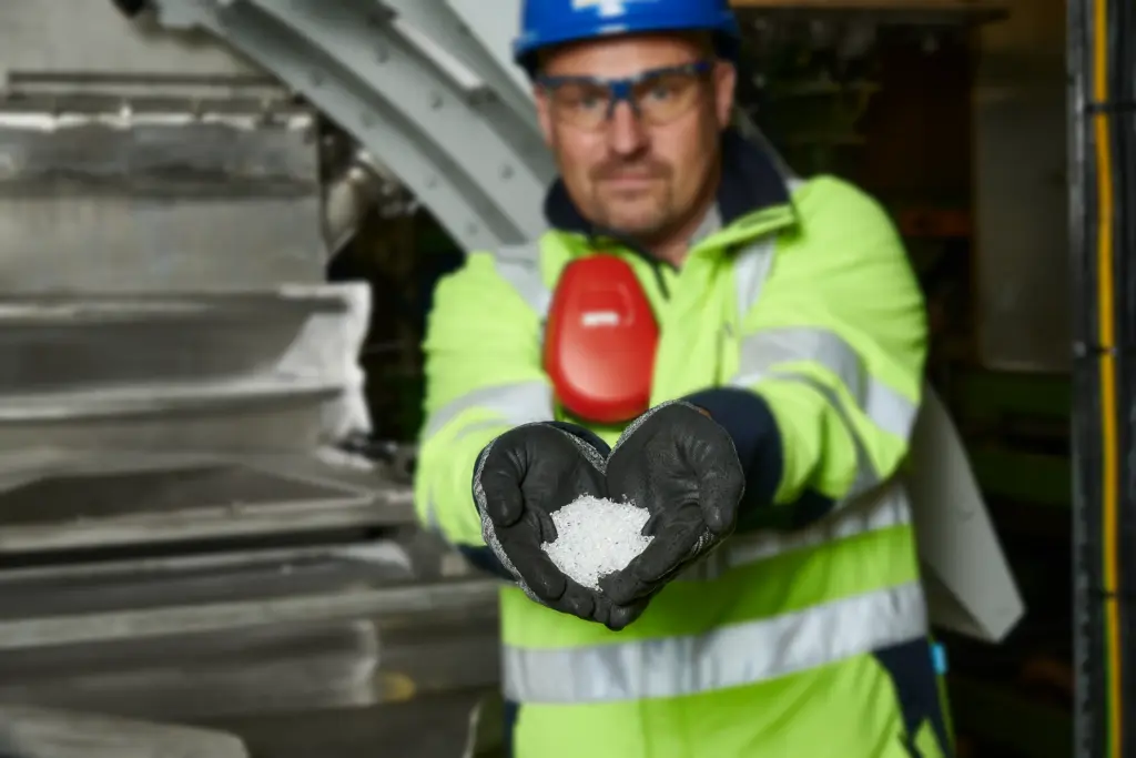 Un addetto alla produzione di un’azienda produttrice di granulato di plastica mostra alla telecamera il granulato appena prodotto e setacciato a scopo di controllo