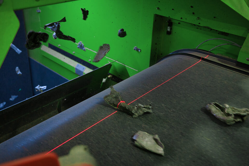 Parti metalliche su un nastro trasportatore in un impianto di riciclaggio con linea laser