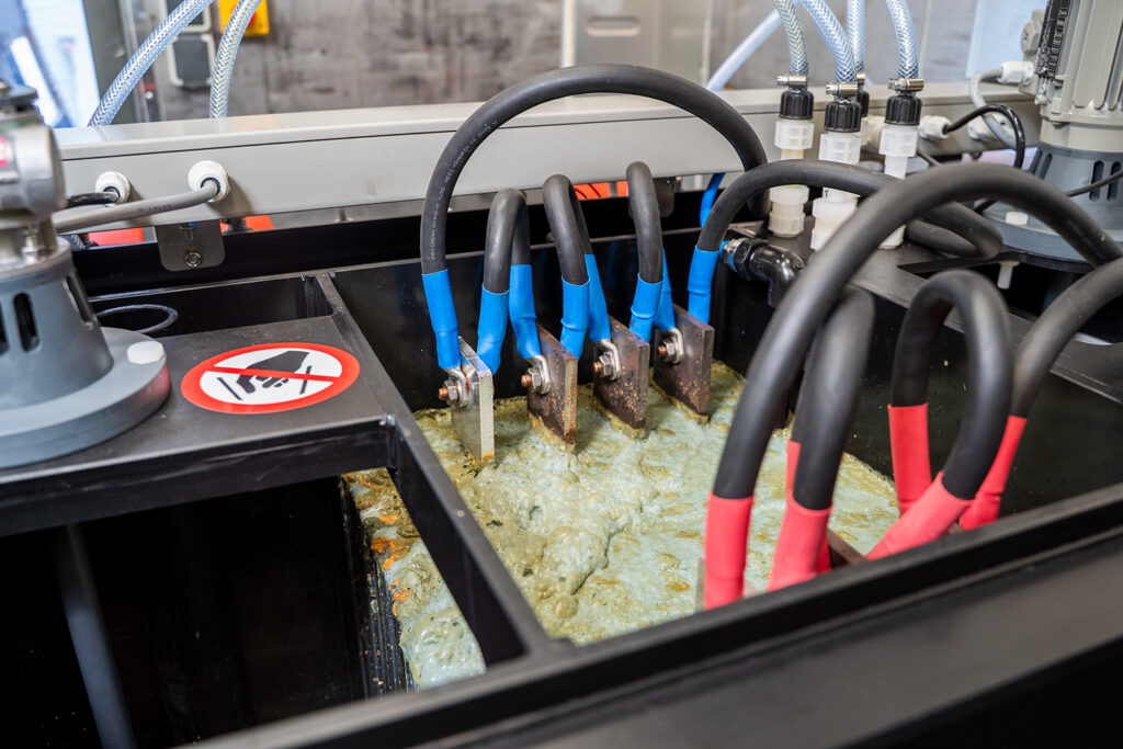 Primo piano di un impianto di elettrocoagulazione in funzione. Mostra le lamelle elettriche presenti nell'acqua contaminata.