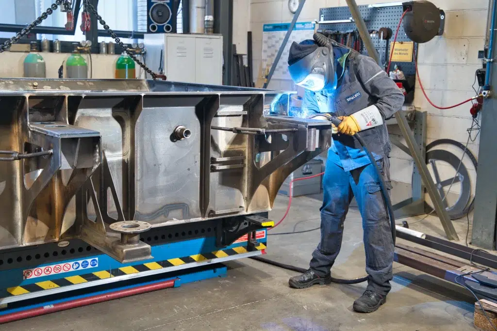 Un operaio sta saldando un grande componente metallico in officina.